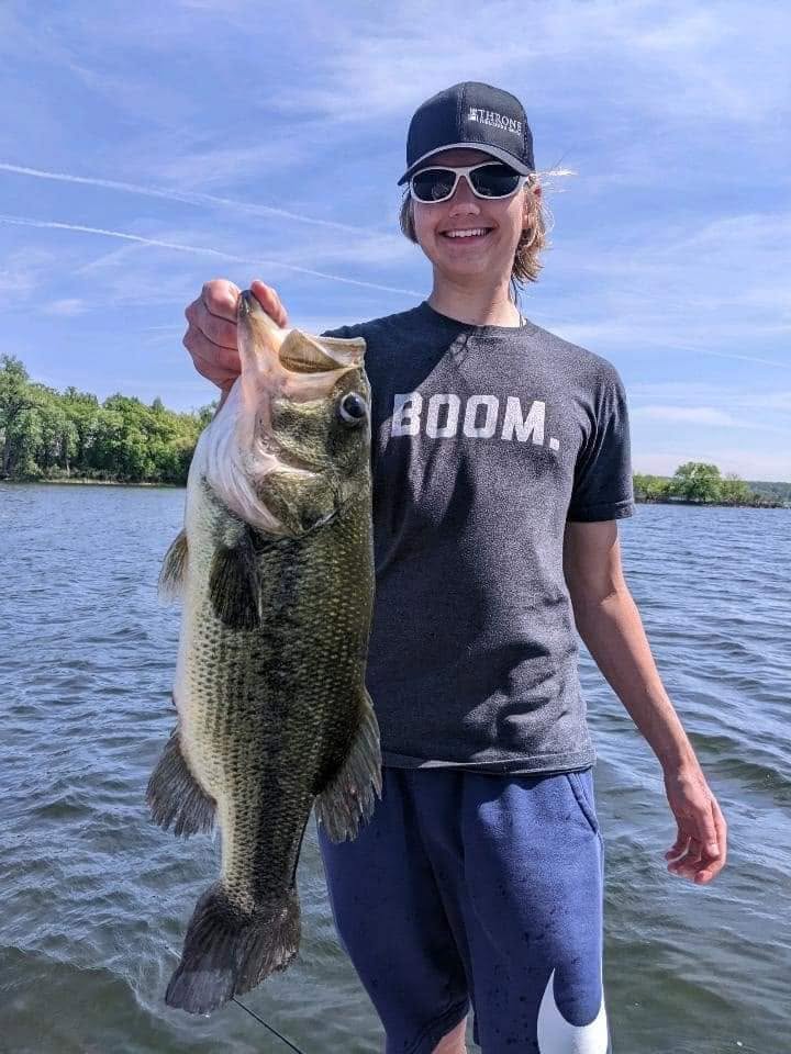 Young angler holding up a large largemouth bass on a sunny lake