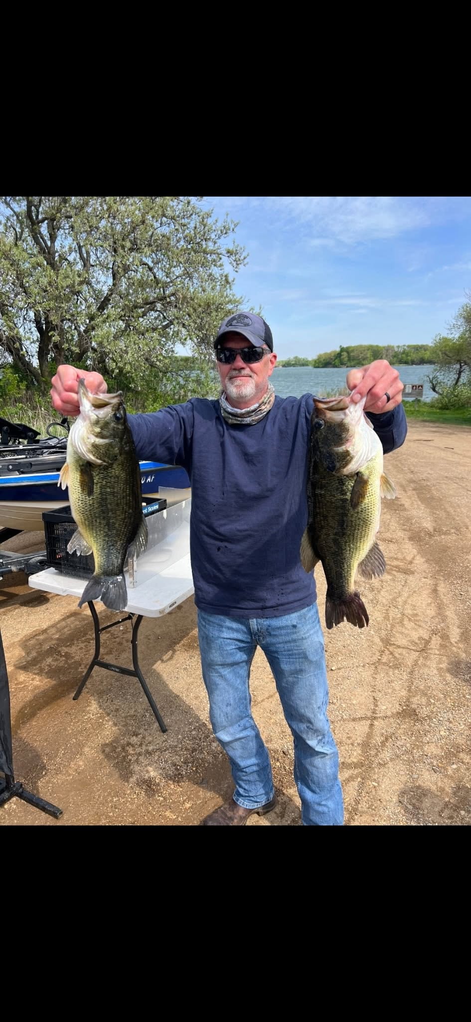 Angler holding two largemouth bass at the boat ramp