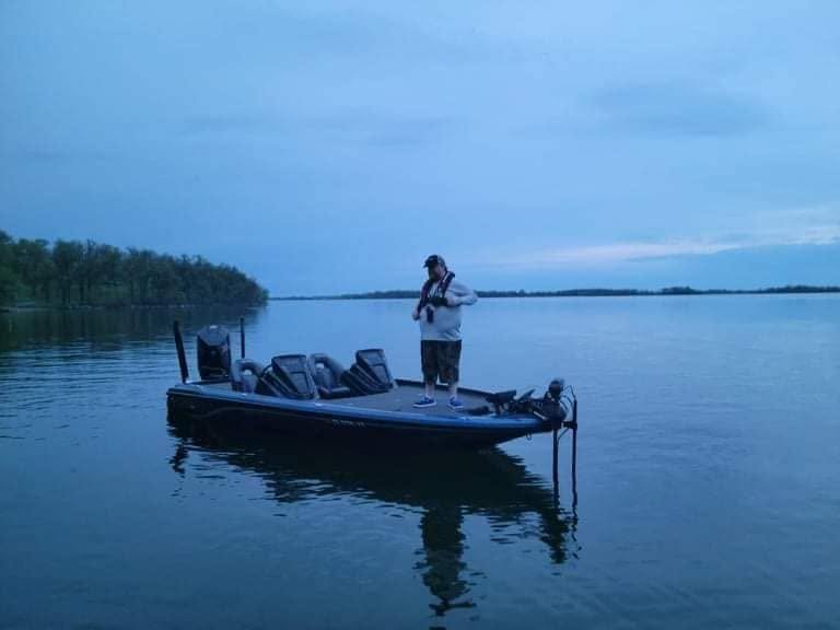 Lone angler fishing from the bow of a bass boat on calm water in the early morning