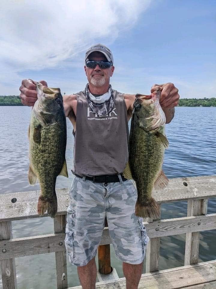 Angler holding up two largemouth bass on a dock