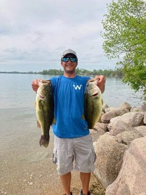 Smiling angler holding two largemouth bass on a rocky shoreline