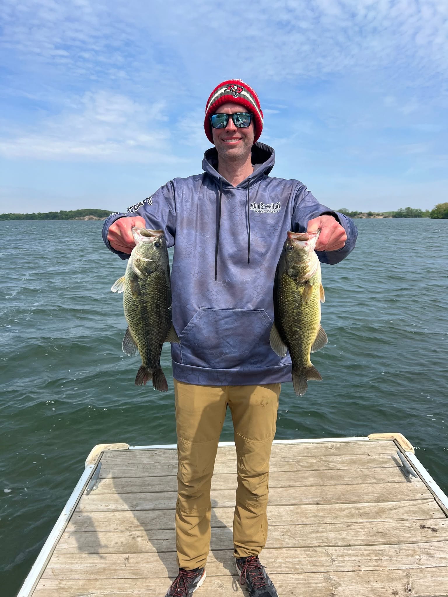 Angler holding two largemouth bass on a dock by a lake
