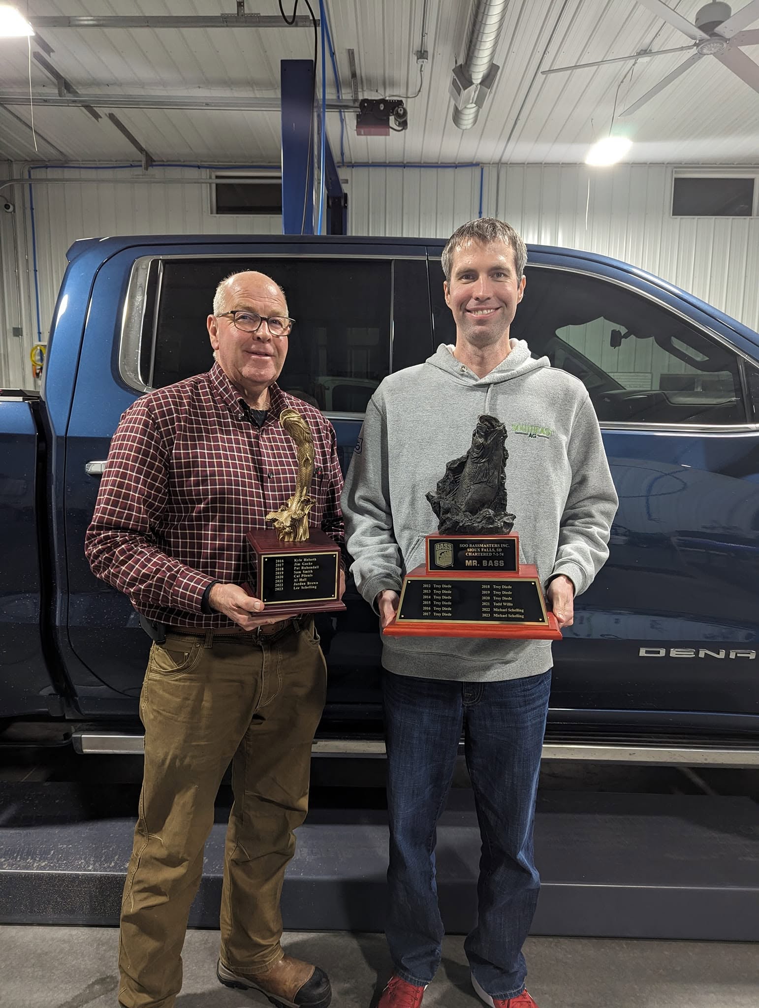 Two members holding fishing trophies and plaques at the club banquet