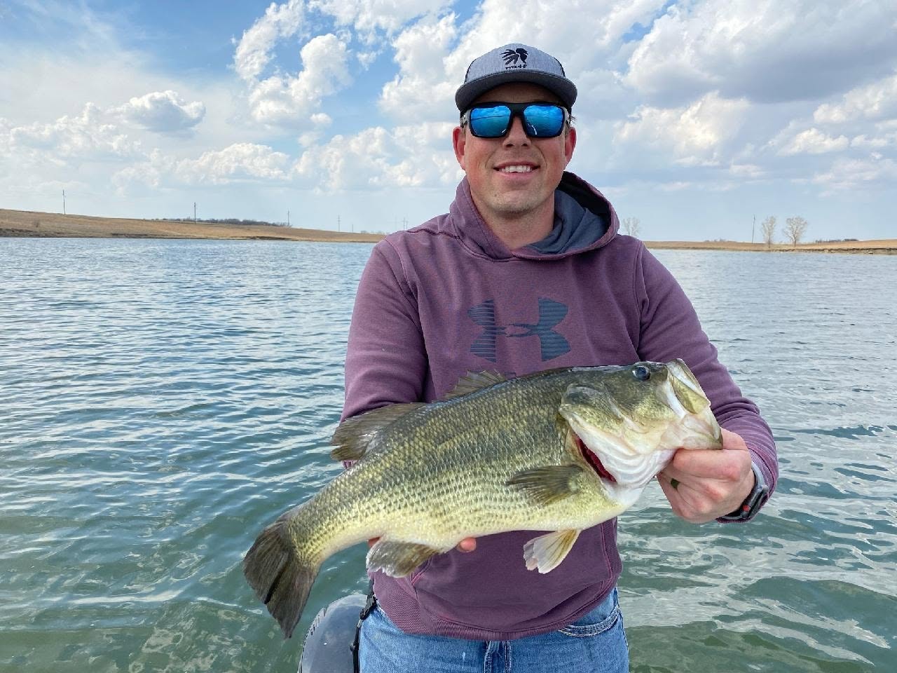 Angler in sunglasses holding a largemouth bass on the reservoir