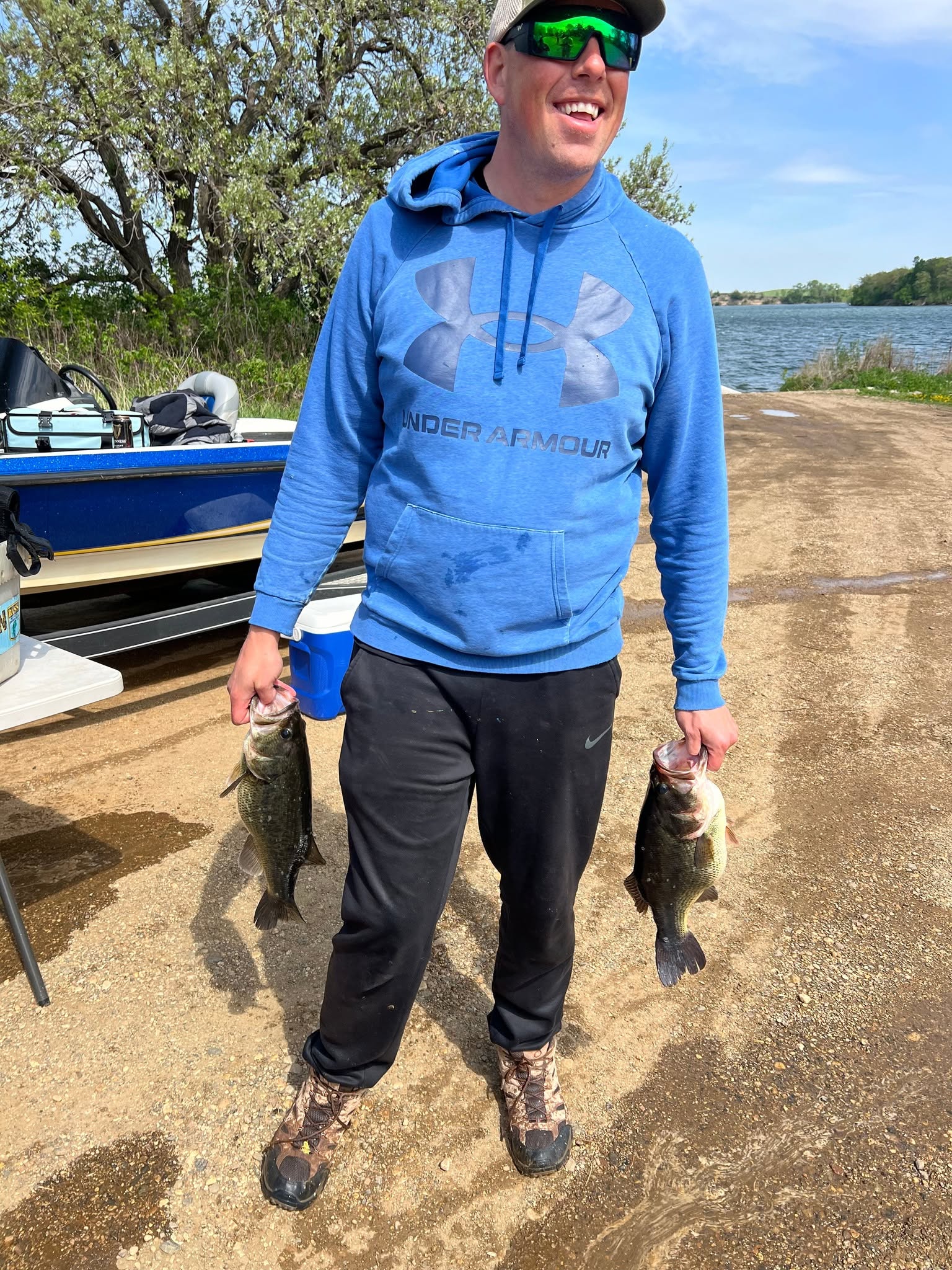 Smiling angler holding two bass at a boat ramp