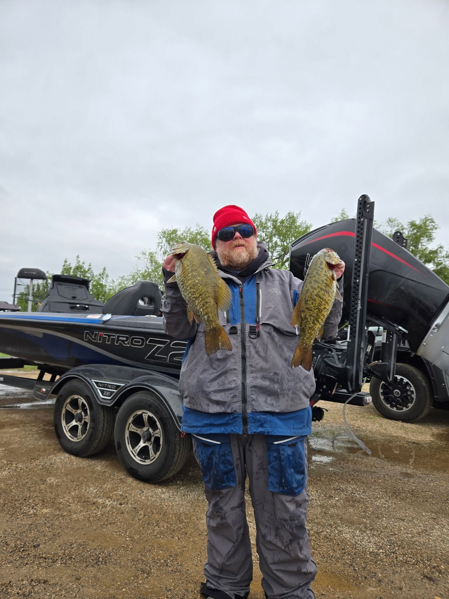 Angler holding two smallmouth bass beside a bass boat