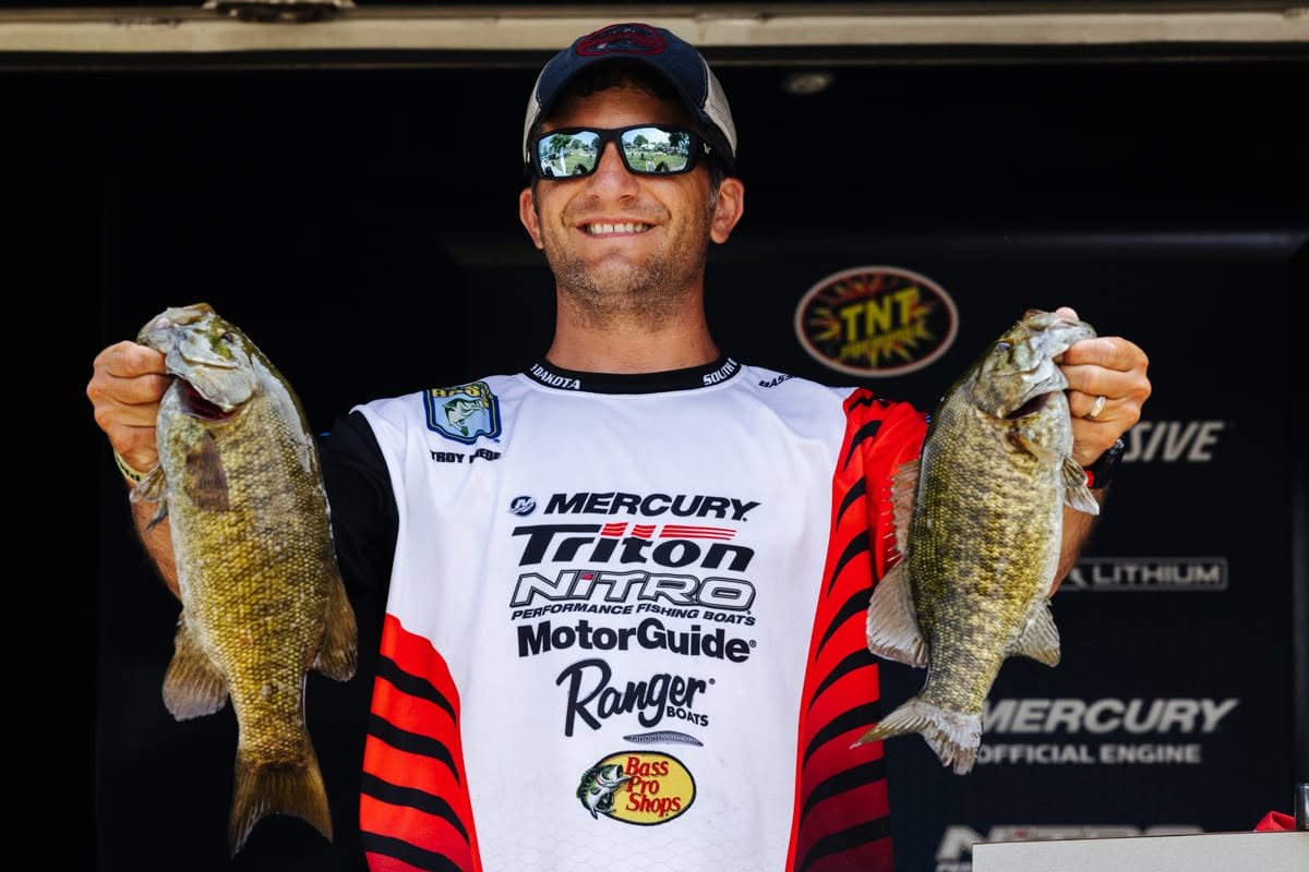 Tournament angler holding up two smallmouth bass on the weigh-in stage
