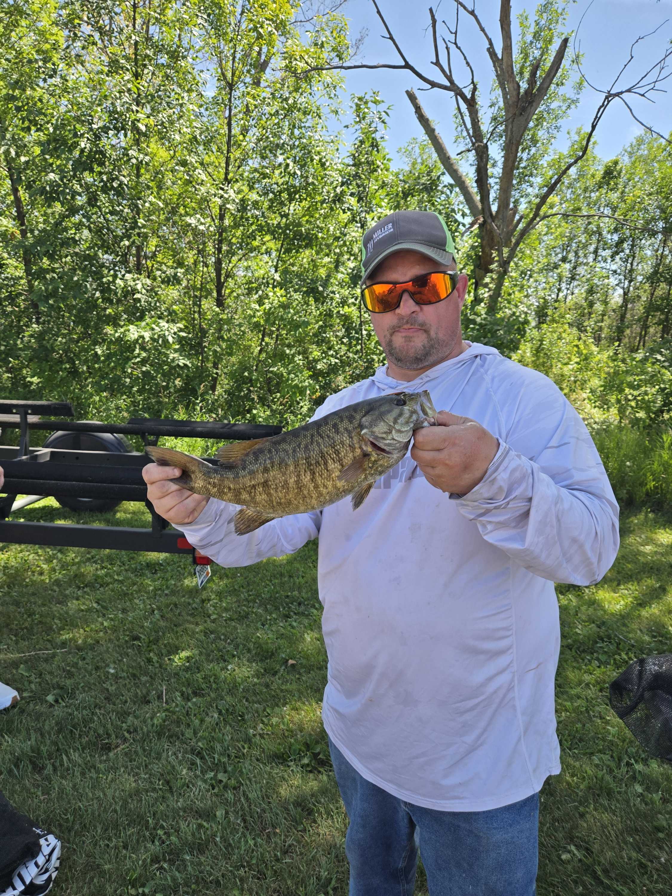 Angler in orange sunglasses showing off a smallmouth bass beside the boat trailer