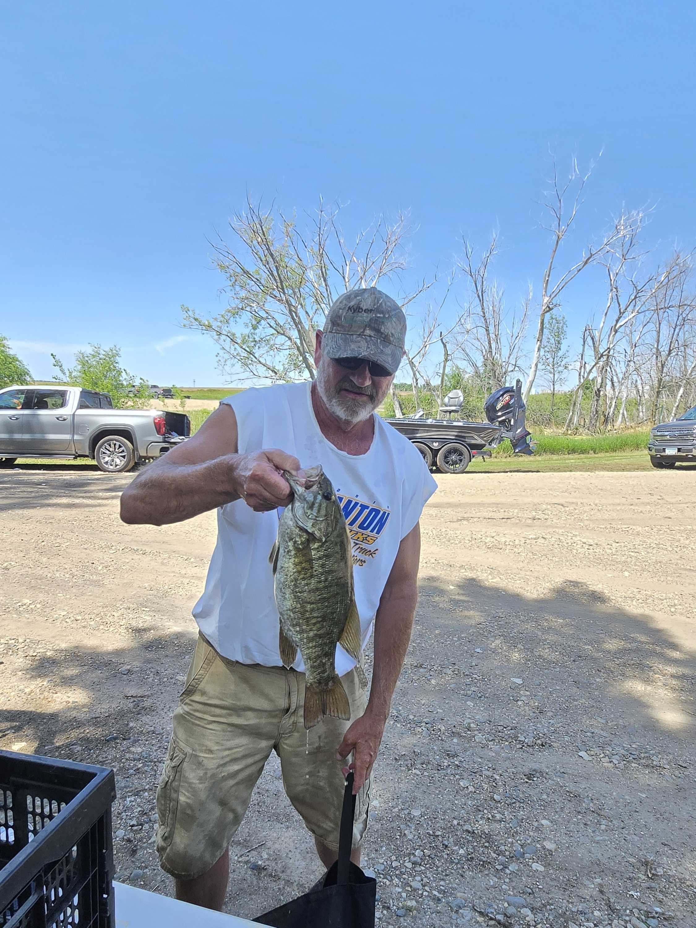 Angler in a camo cap holding a smallmouth bass at the weigh station