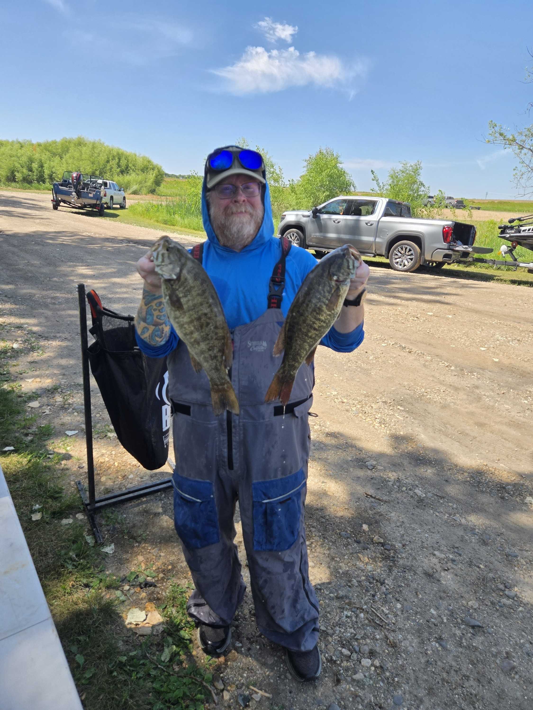 Angler in bibs holding two smallmouth bass by the weigh-in bag stand