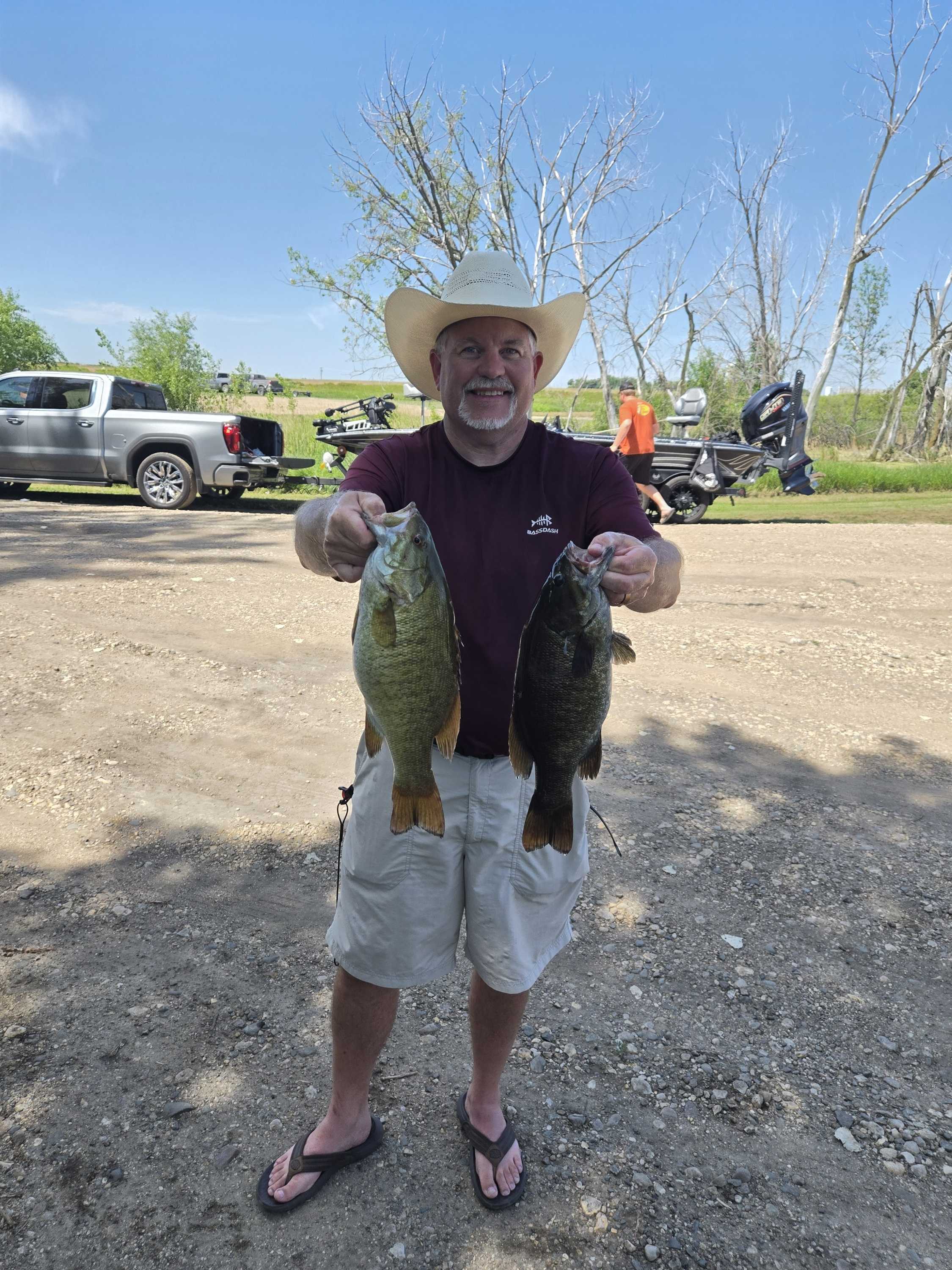 Angler in a cowboy hat holding two smallmouth bass on a sunny day at Blue Dog Lake