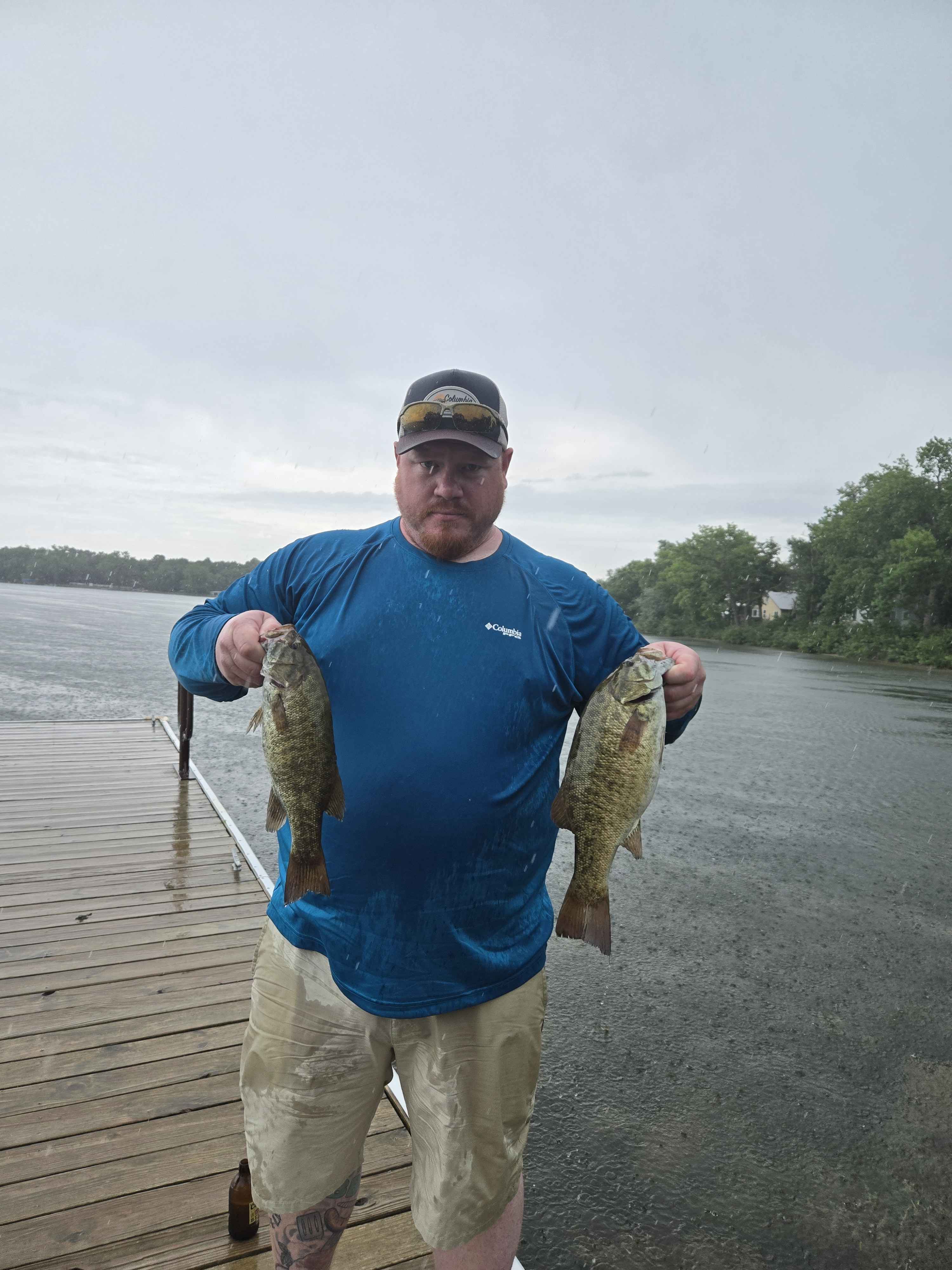 Angler holding two smallmouth bass on the dock in the rain at Enemy Swim